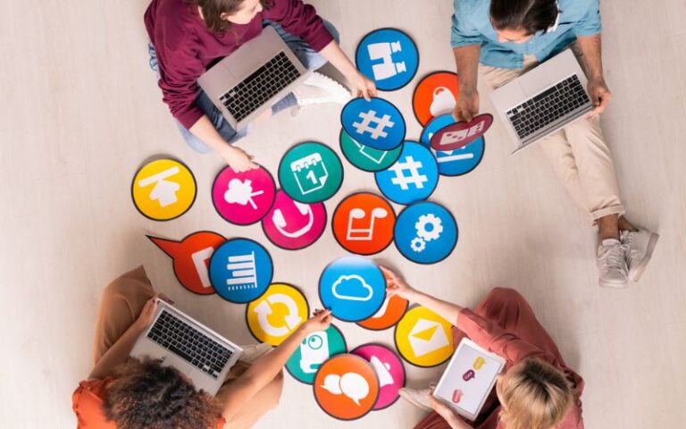 Group of marketers sitting on the floor with laptops, organizing colorful icons of online marketing tools and social media platforms, representing essential resources for affiliate marketing.